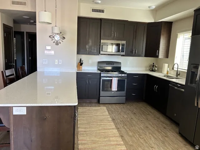 Kitchen featuring a peninsula, stainless steel appliances, a kitchen bar, decorative light fixtures, and light stone countertops