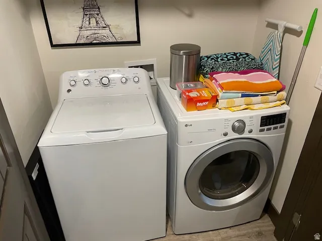 Laundry area with washing machine and clothes dryer and light wood-style flooring