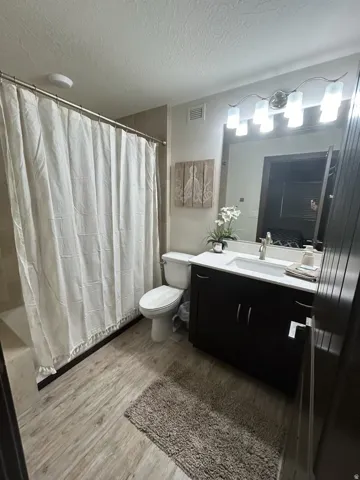 Full bathroom with vanity, a textured ceiling, light wood-style floors, and shower / tub combo