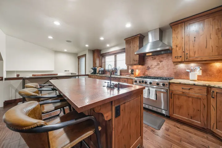 Kitchen with a breakfast bar area, high end stainless steel range oven, wood finish cabinetry, light wood-type flooring, and backsplash