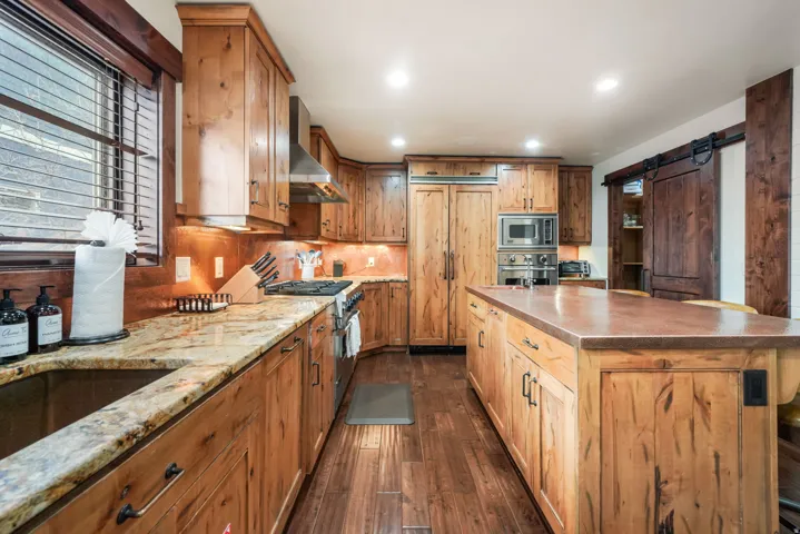 Kitchen with a barn door, built in appliances, dark wood-style flooring, recessed lighting, and a center island