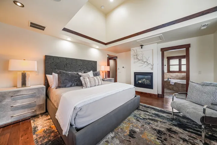 Bedroom with dark wood-type flooring, a glass covered fireplace, and a raised ceiling