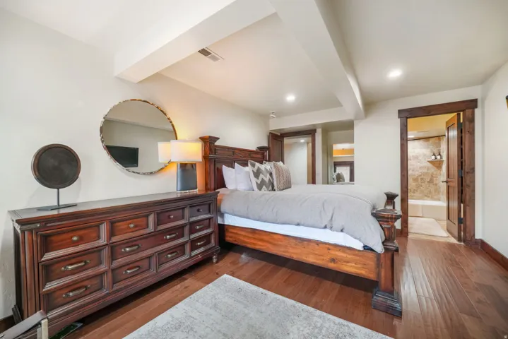 Bedroom featuring dark wood-style flooring, ensuite bath, and beam ceiling