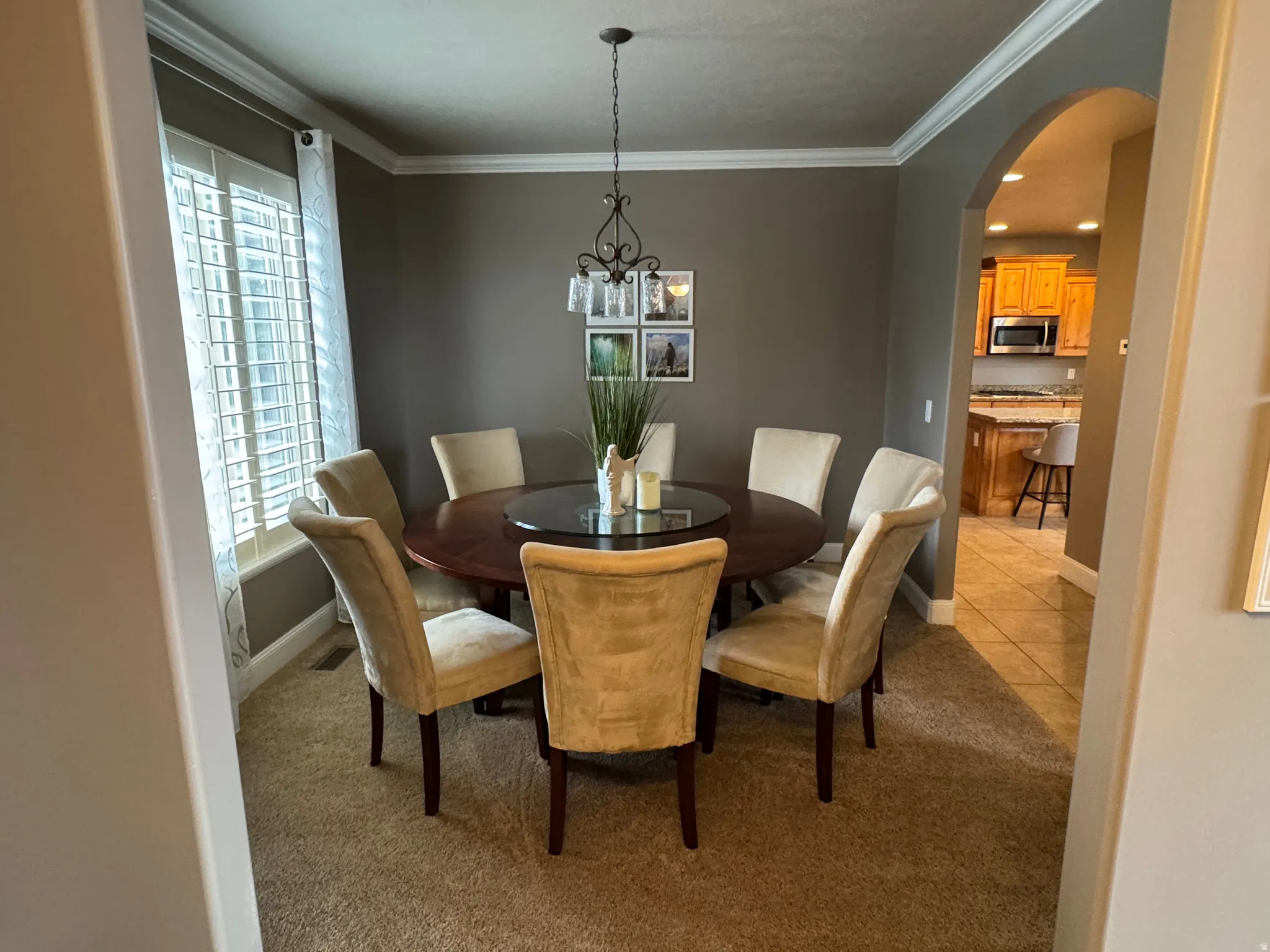 Dining room featuring light carpet, a chandelier, ornamental molding, and arched walkways