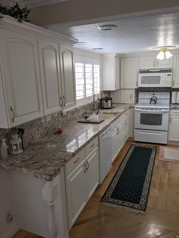 Kitchen with white appliances, white cabinets, light wood-style flooring, light stone counters, and a textured ceiling
