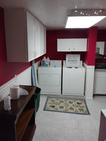 Laundry room with wainscoting, cabinet space, washing machine and dryer, a textured ceiling, and wood walls