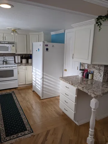 Kitchen with tasteful backsplash, white appliances, light wood finished floors, white cabinetry, and ornamental molding