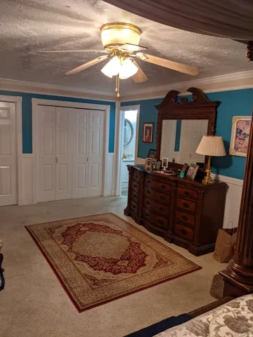 Bedroom featuring crown molding, a closet, a wainscoted wall, light colored carpet, and a ceiling fan