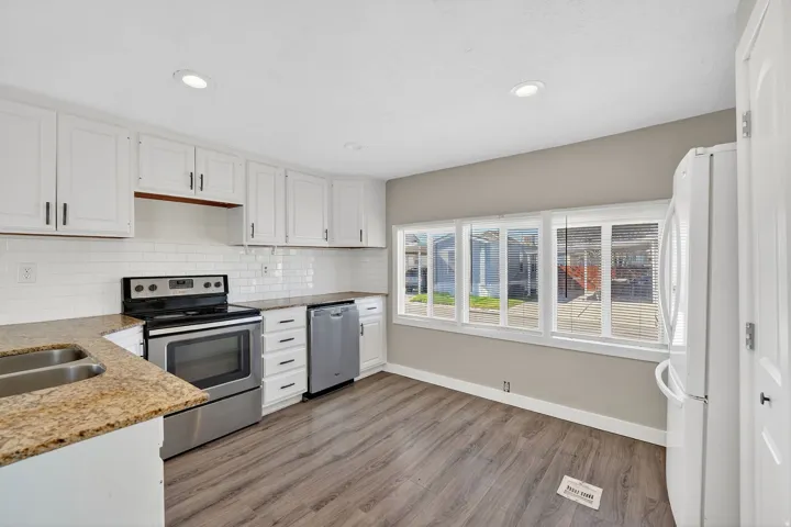 Kitchen with stainless steel appliances, light stone countertops, white cabinets, dark wood finished floors, and recessed lighting