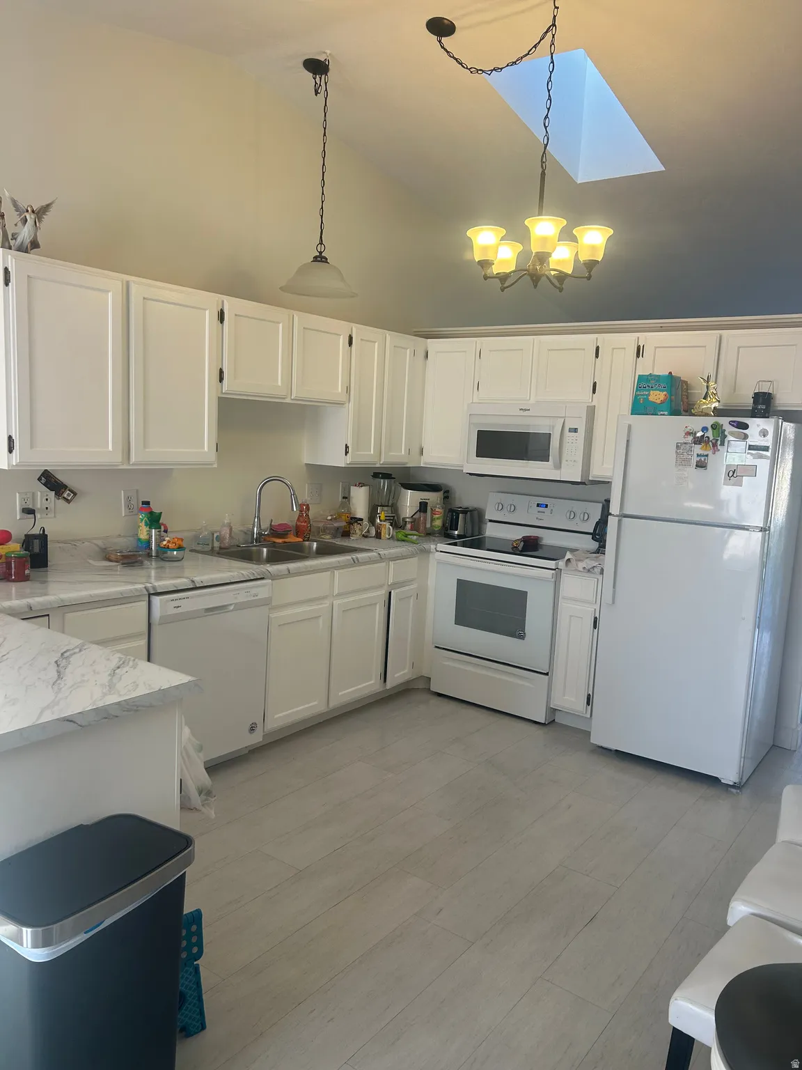 Kitchen with white appliances, white cabinetry, a skylight, hanging lights, and vaulted ceiling
