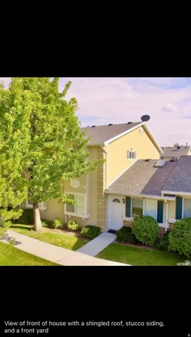 Traditional-style house featuring a front lawn, stucco siding, and a shingled roof