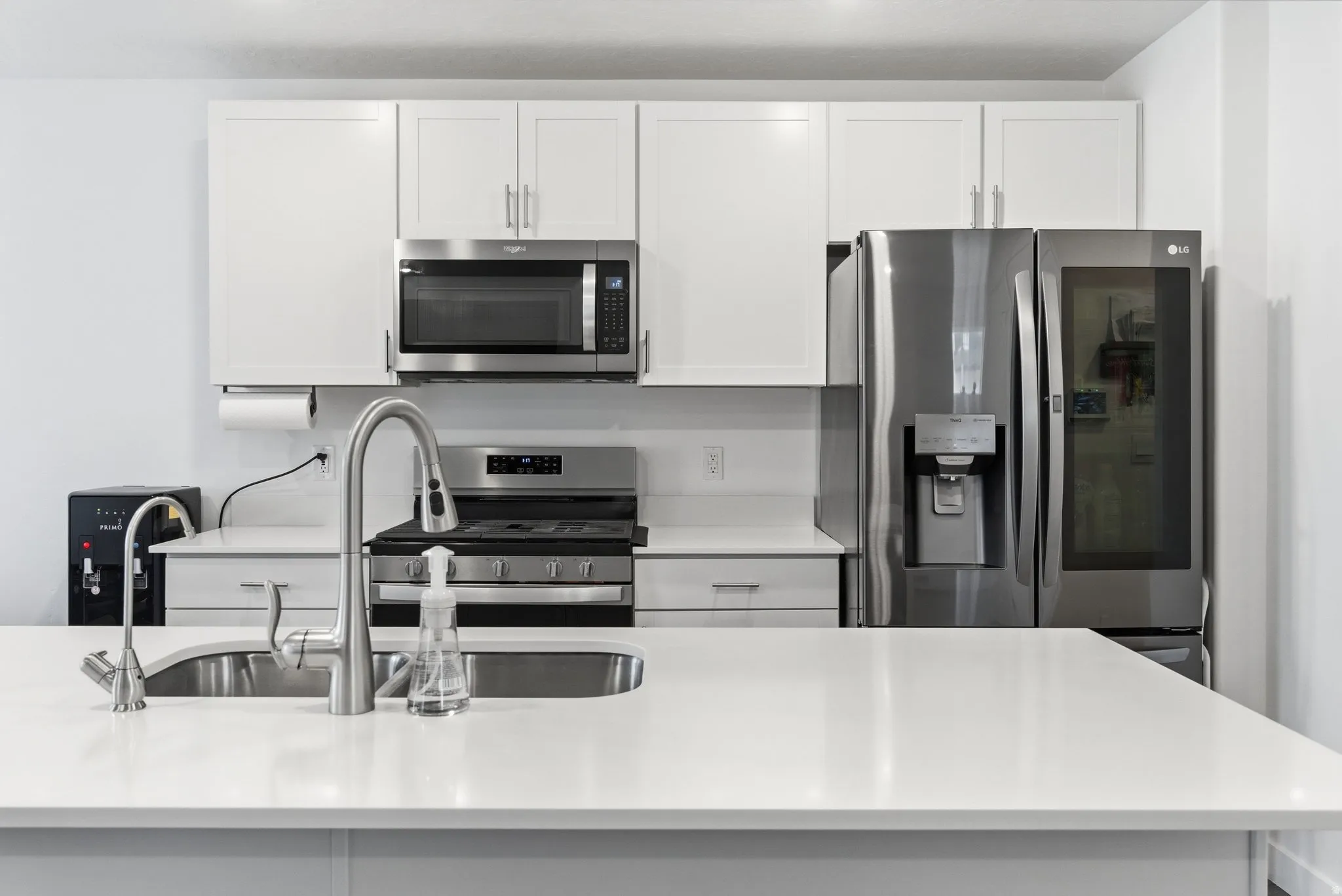 Kitchen featuring stainless steel appliances, white cabinets, and light stone counters