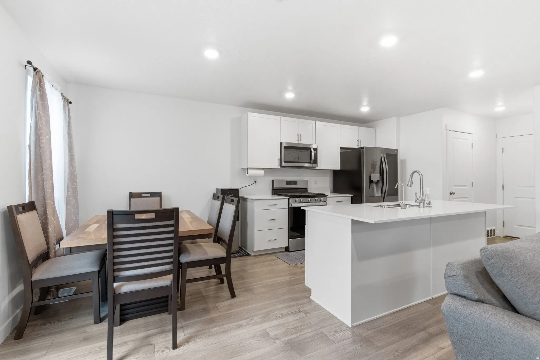 Kitchen featuring stainless steel appliances, white cabinetry, a kitchen island with sink, light wood-style flooring, and recessed lighting