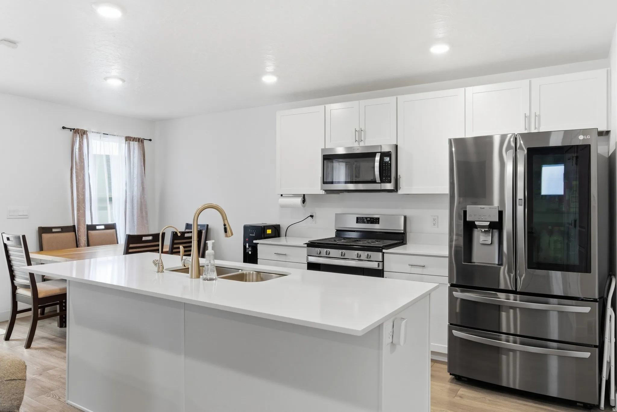 Kitchen featuring stainless steel appliances, white cabinets, an island with sink, light wood-style floors, and recessed lighting