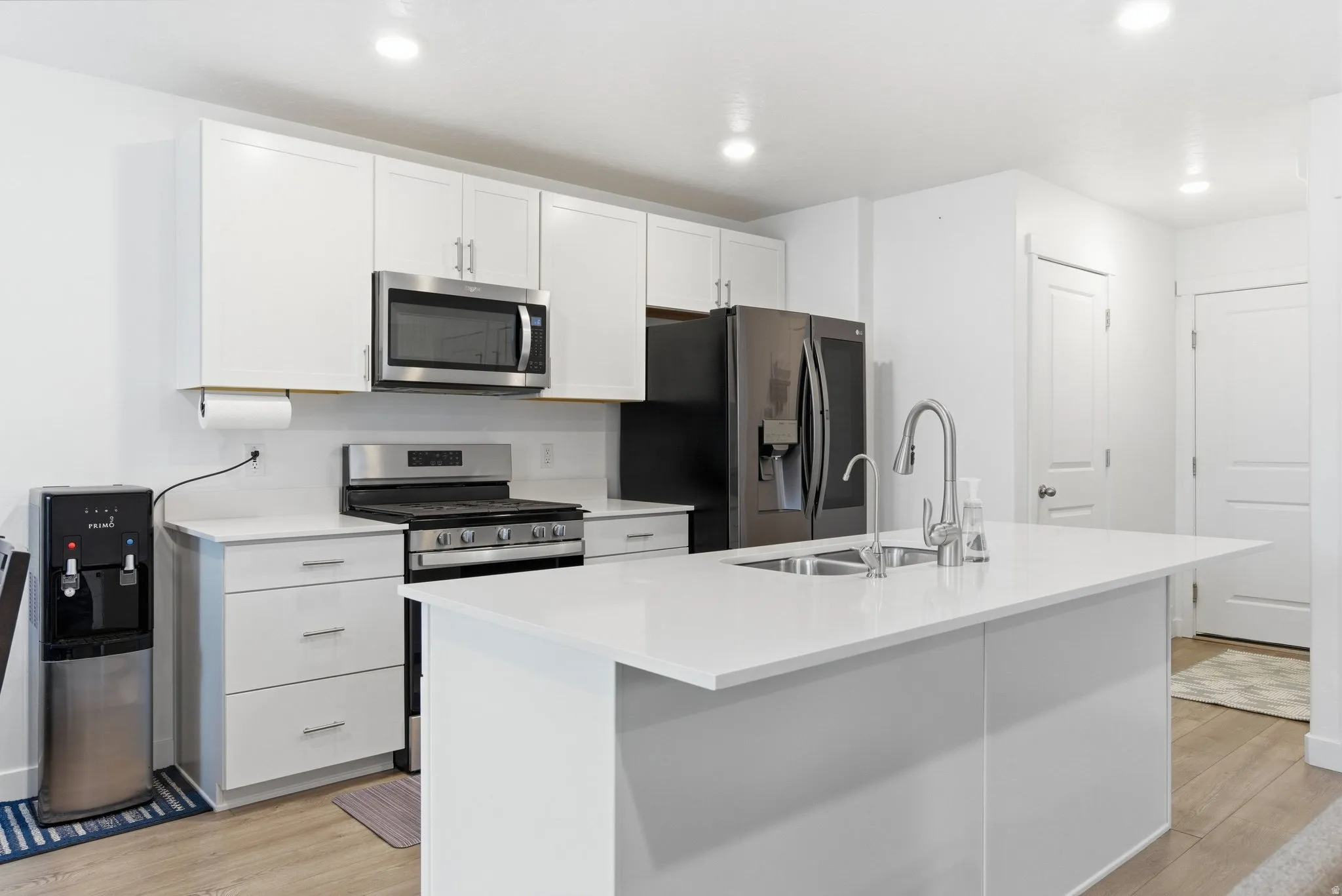 Kitchen with stainless steel appliances, white cabinets, a center island with sink, light wood-style flooring, and recessed lighting