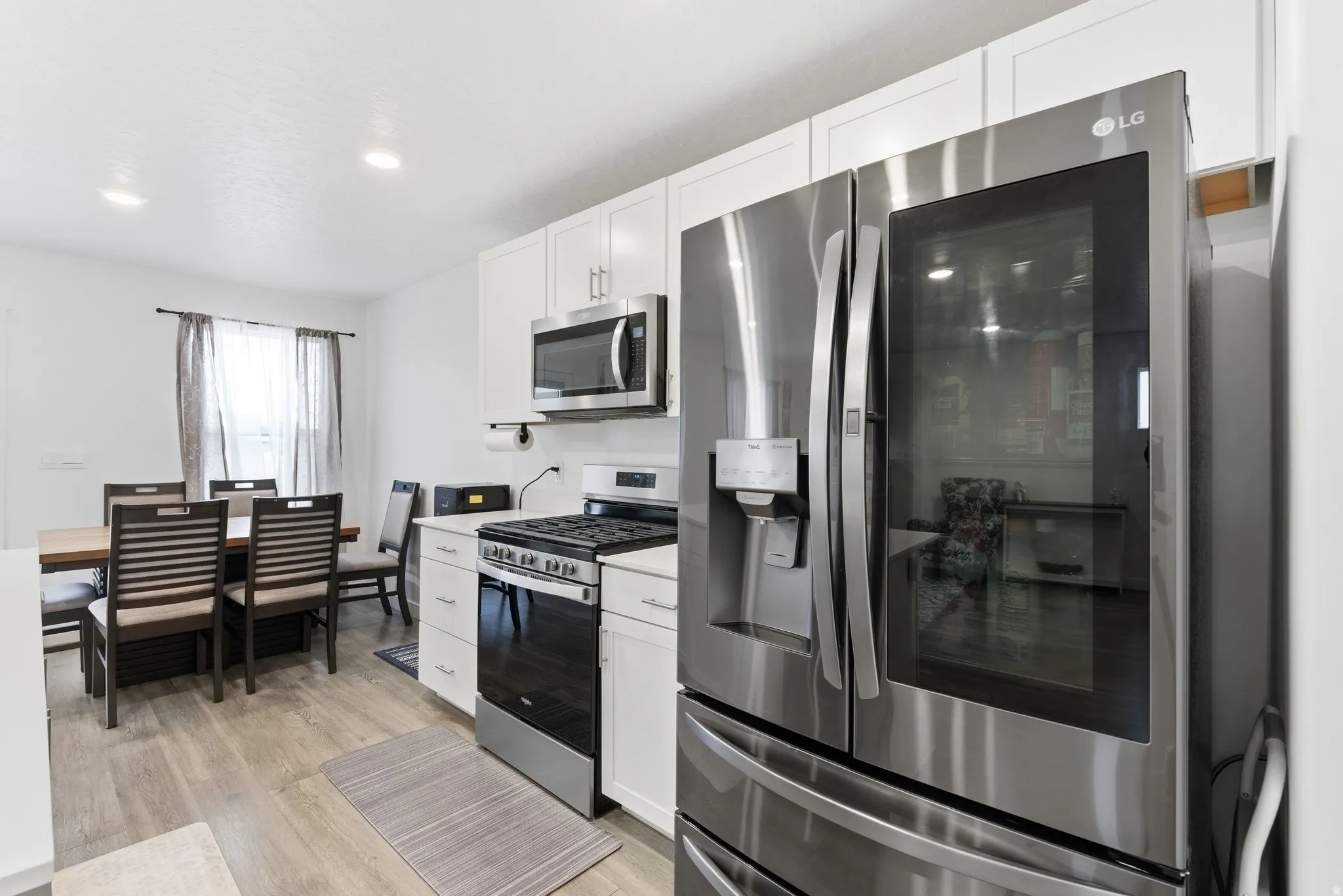 Kitchen featuring stainless steel appliances, light countertops, white cabinetry, light wood-style flooring, and recessed lighting