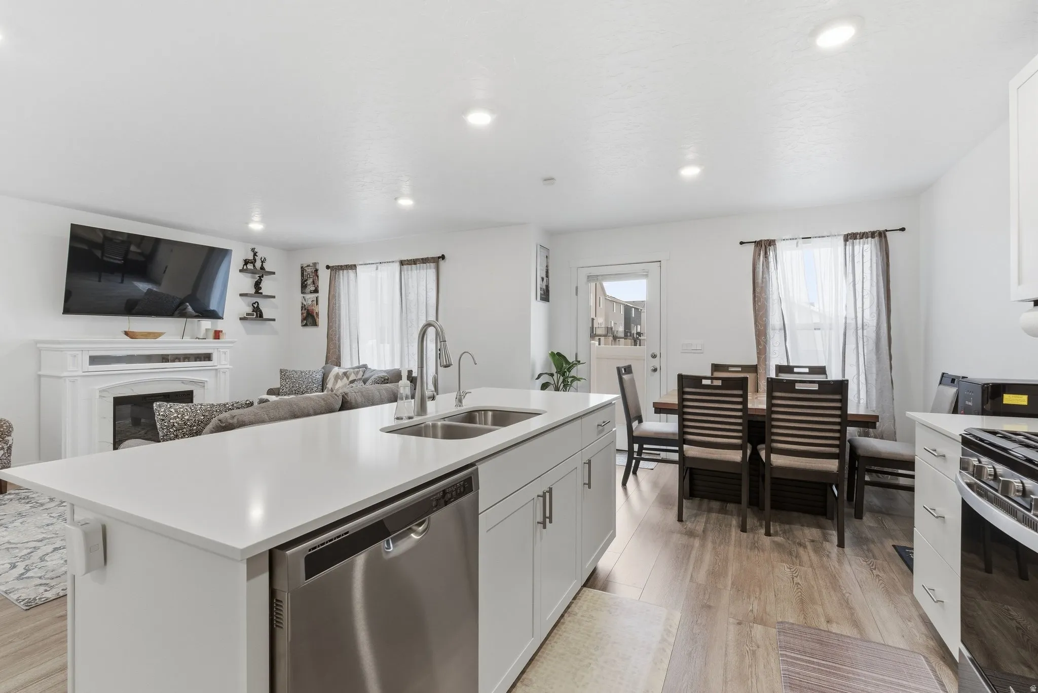 Kitchen featuring stainless steel dishwasher, open floor plan, a center island with sink, light wood-type flooring, and white cabinetry