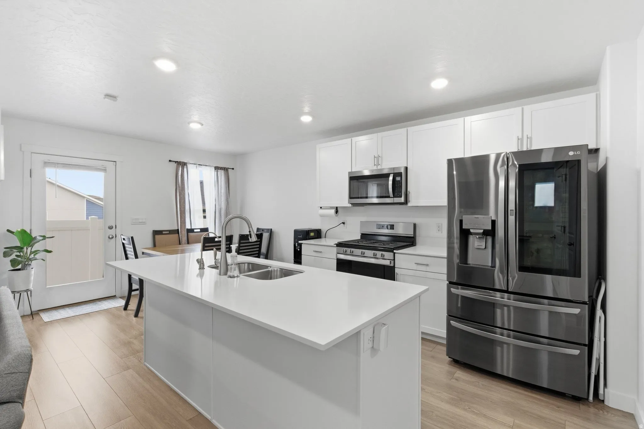 Kitchen featuring stainless steel appliances, white cabinets, an island with sink, light wood-style flooring, and recessed lighting