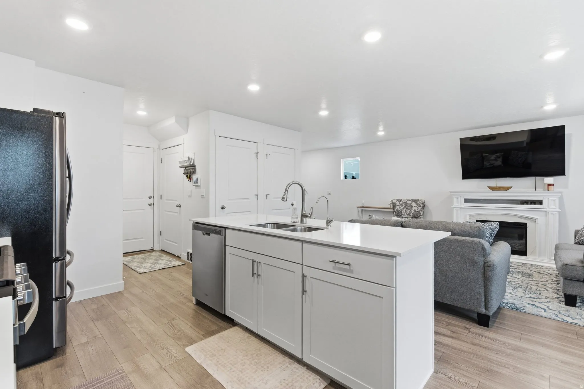 Kitchen with open floor plan, a fireplace, a kitchen island with sink, light wood-type flooring, and stainless steel appliances