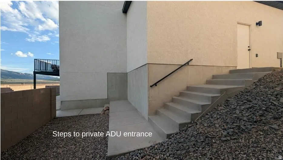 Exterior stucco finish, concrete stairway with metal handrail, and ground-level rock landscaping