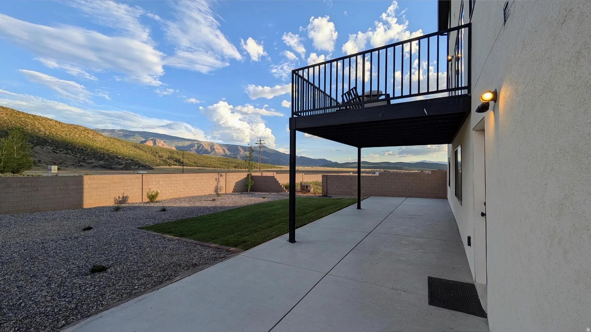 Rear concrete patio with an overhead balcony featuring black metal railings and supports
