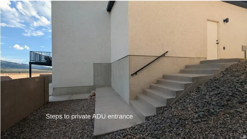 Exterior stucco finish, concrete stairway with metal handrail, and ground-level rock landscaping