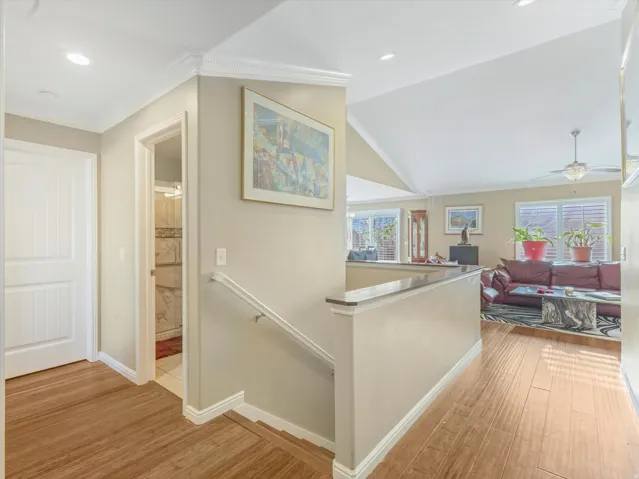 Hallway with an upstairs landing, crown molding, light wood finished floors, vaulted ceiling, and plenty of natural light
