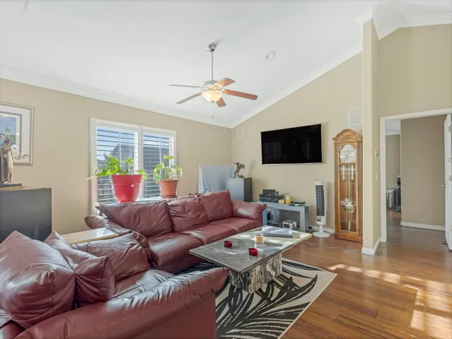 Living room featuring crown molding, lofted ceiling, wood finished floors, and ceiling fan