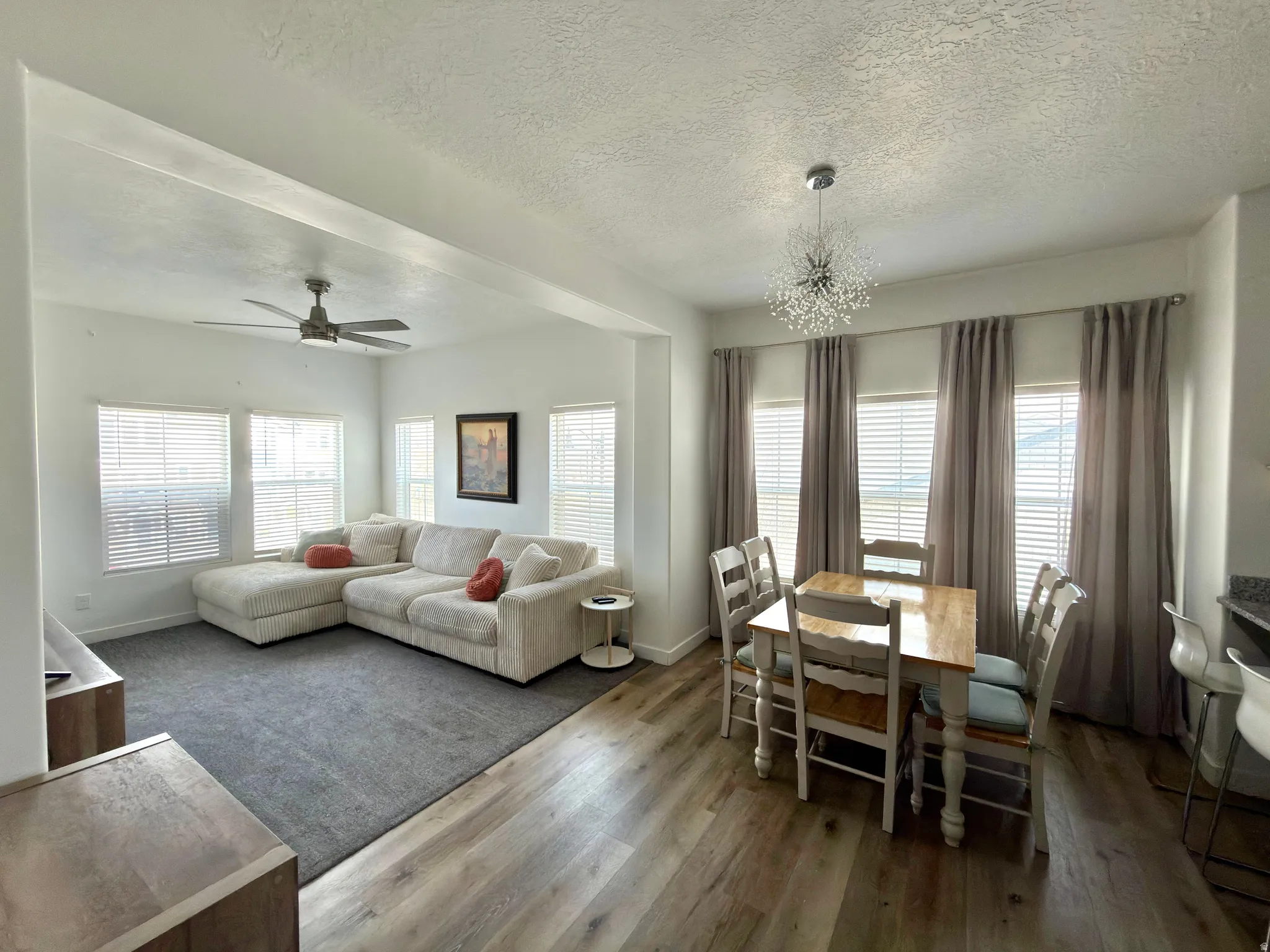 Living room with dark wood-style flooring, a textured ceiling, a ceiling fan, a chandelier, and healthy amount of natural light