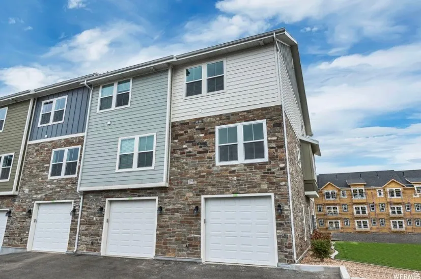 Back of property featuring stone siding, a garage, and driveway