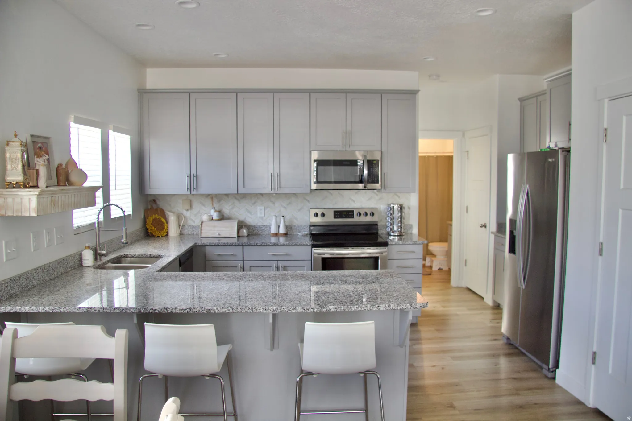 Kitchen with gray cabinetry, a peninsula, stainless steel appliances, light stone counters, and recessed lighting