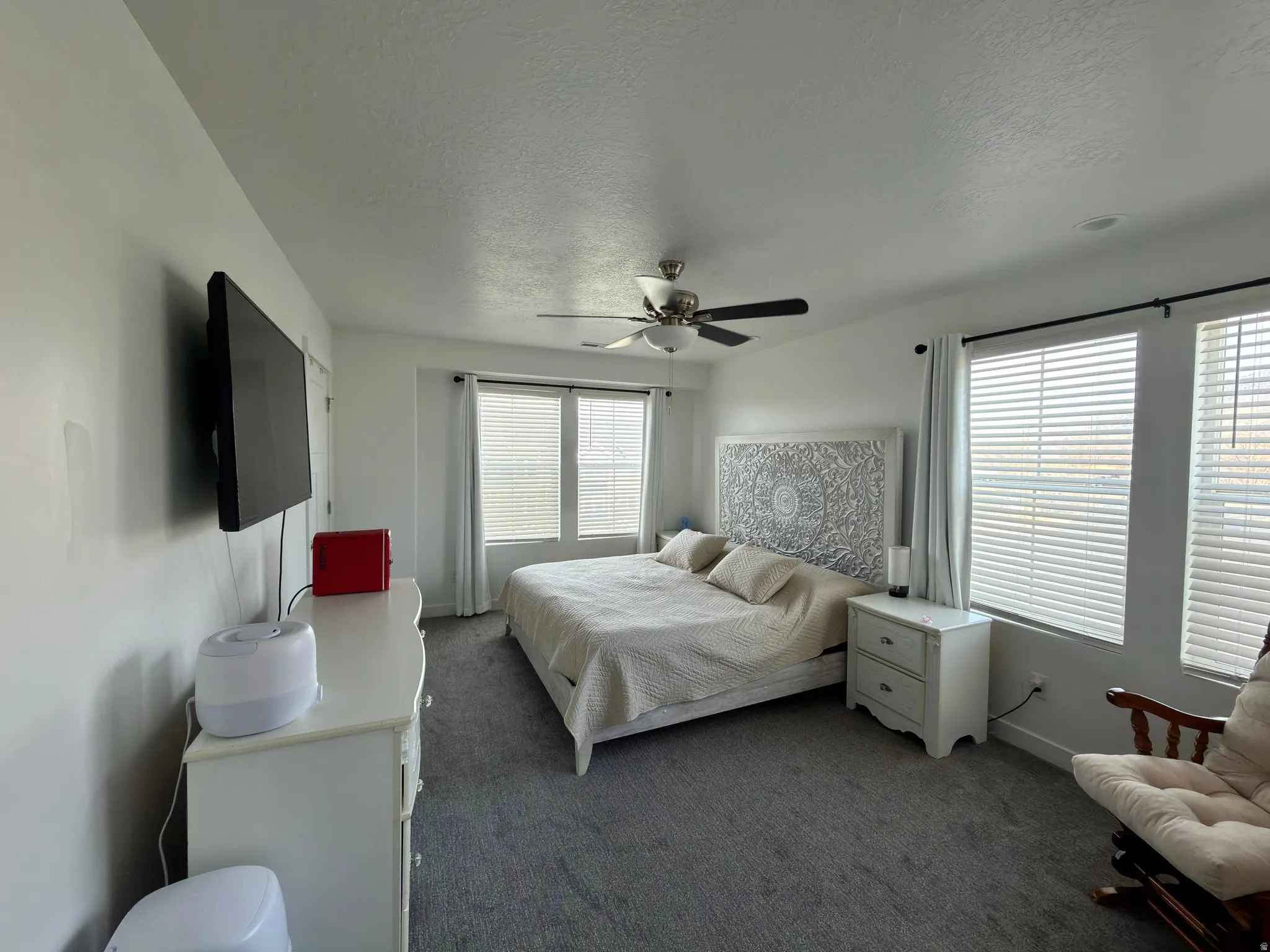 Bedroom with a textured ceiling, multiple windows, a ceiling fan, and dark colored carpet