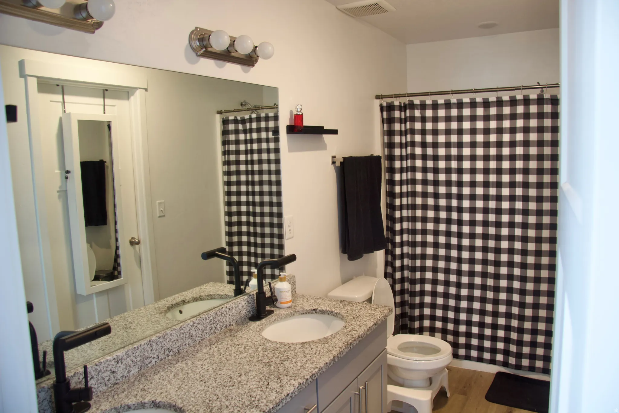 Full bathroom featuring double vanity, a shower with shower curtain, and light wood-style flooring