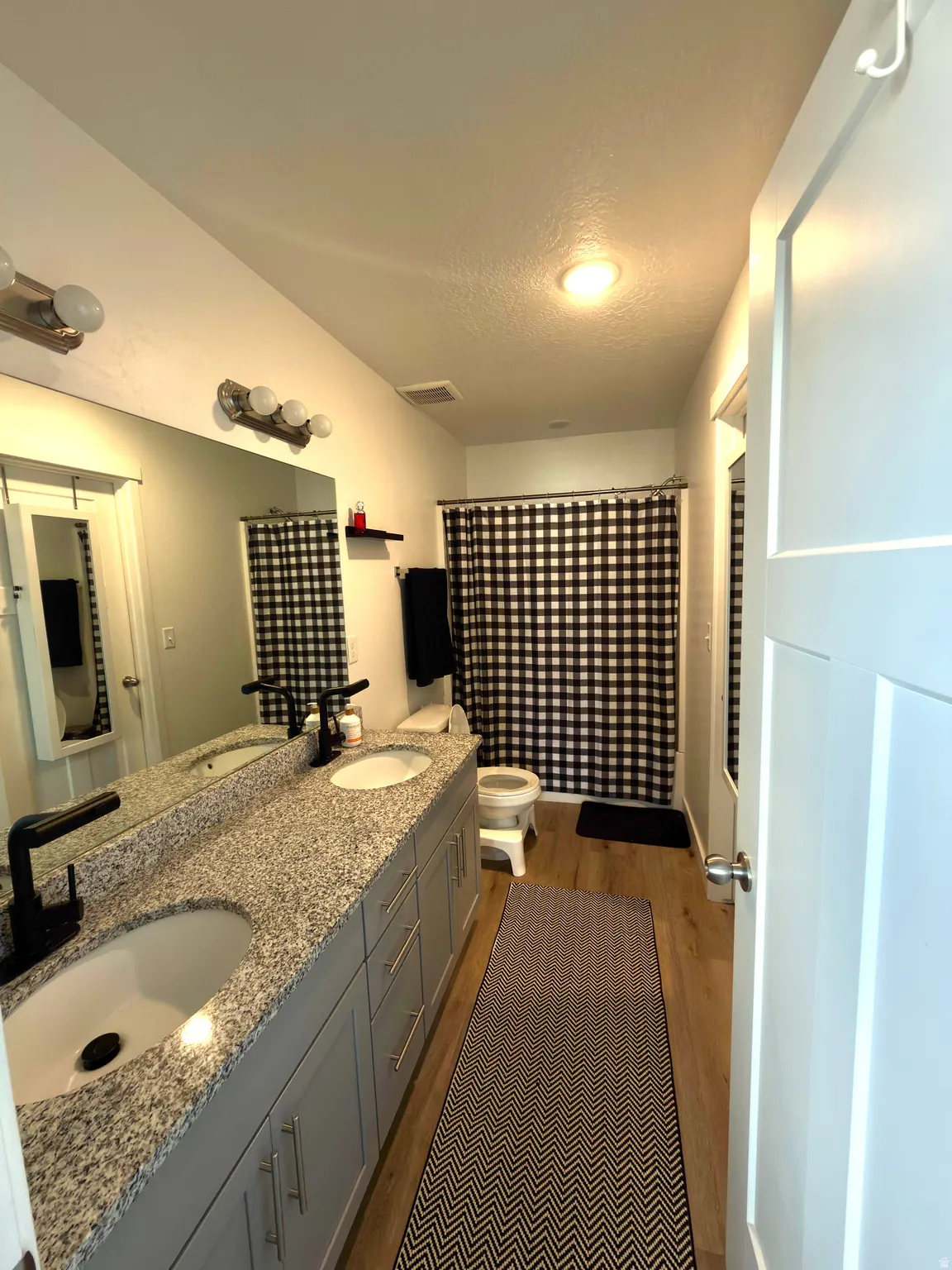 Full bathroom with double vanity, dark wood-style flooring, and a textured ceiling