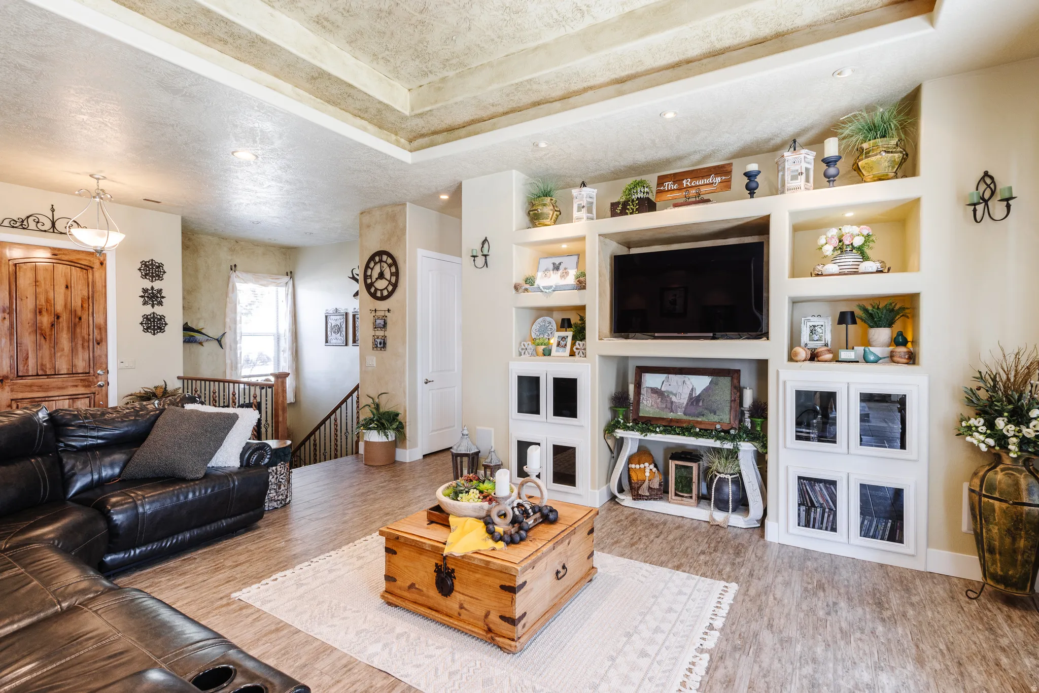 Living room featuring built in shelves, light wood-style flooring, a raised ceiling, recessed lighting, and a textured ceiling