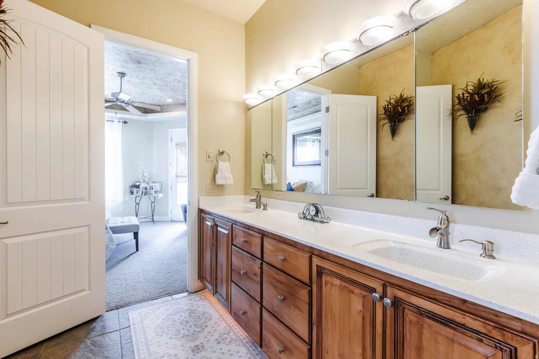 Bathroom with double vanity, light colored carpet, and ceiling fan