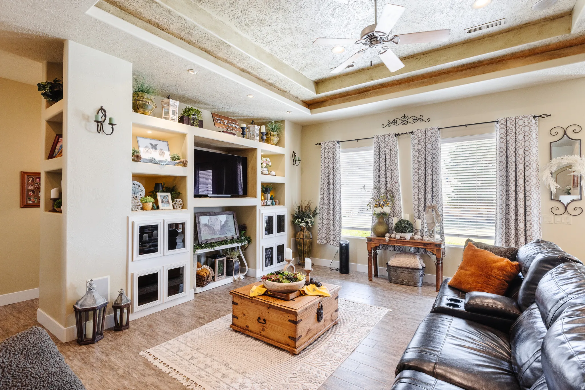Living room featuring ceiling fan, a textured ceiling, light wood-style flooring, a raised ceiling, and built in features