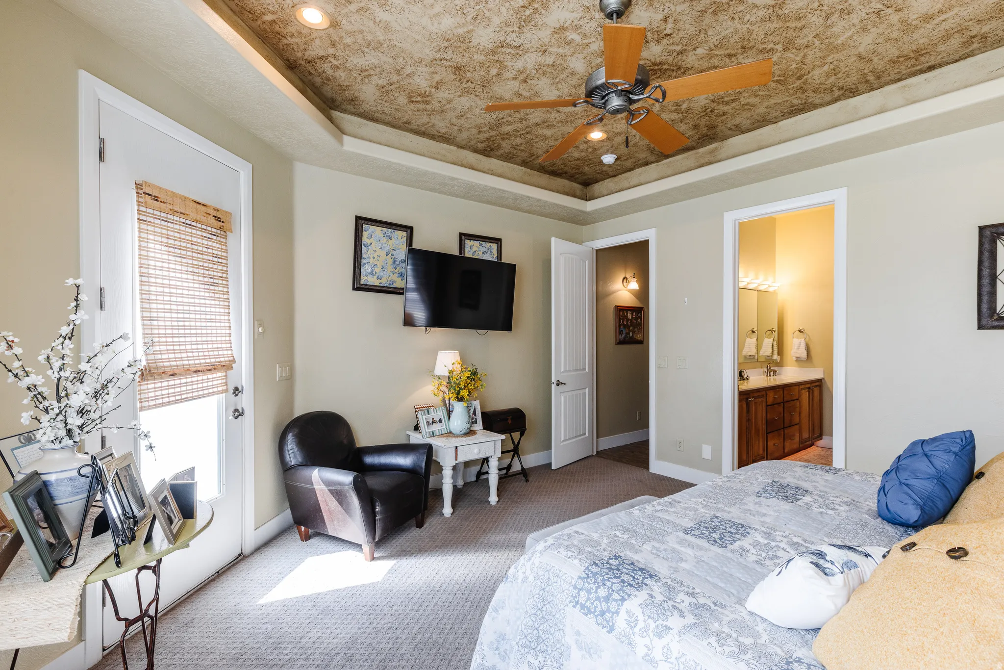 Bedroom featuring carpet floors, a raised ceiling, ensuite bathroom, and ceiling fan