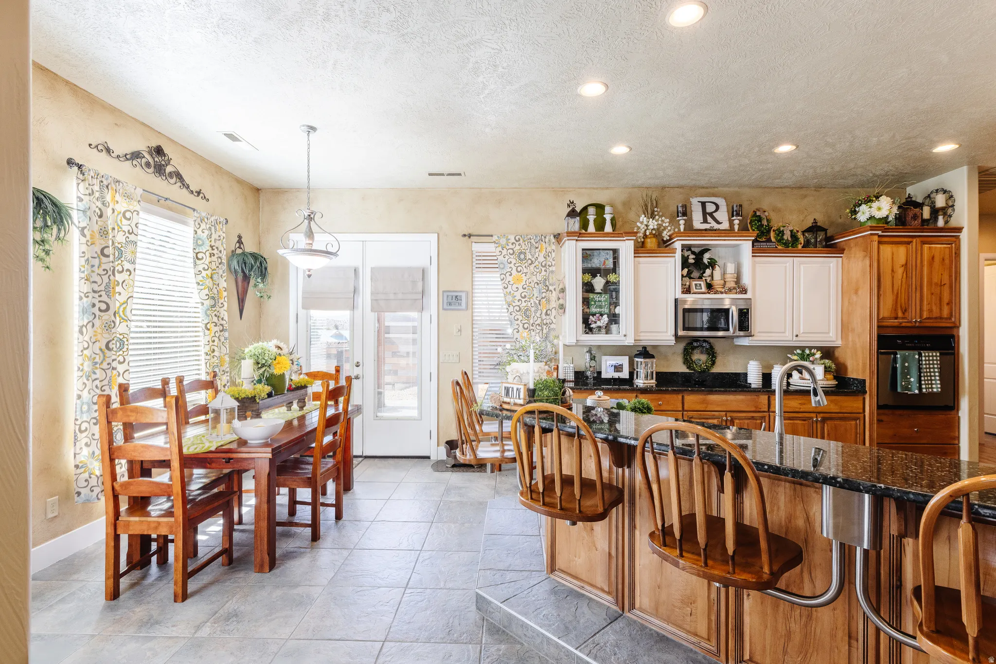 Kitchen featuring black appliances, dark stone counters, pendant lighting, wood finish cabinetry, and a breakfast bar area