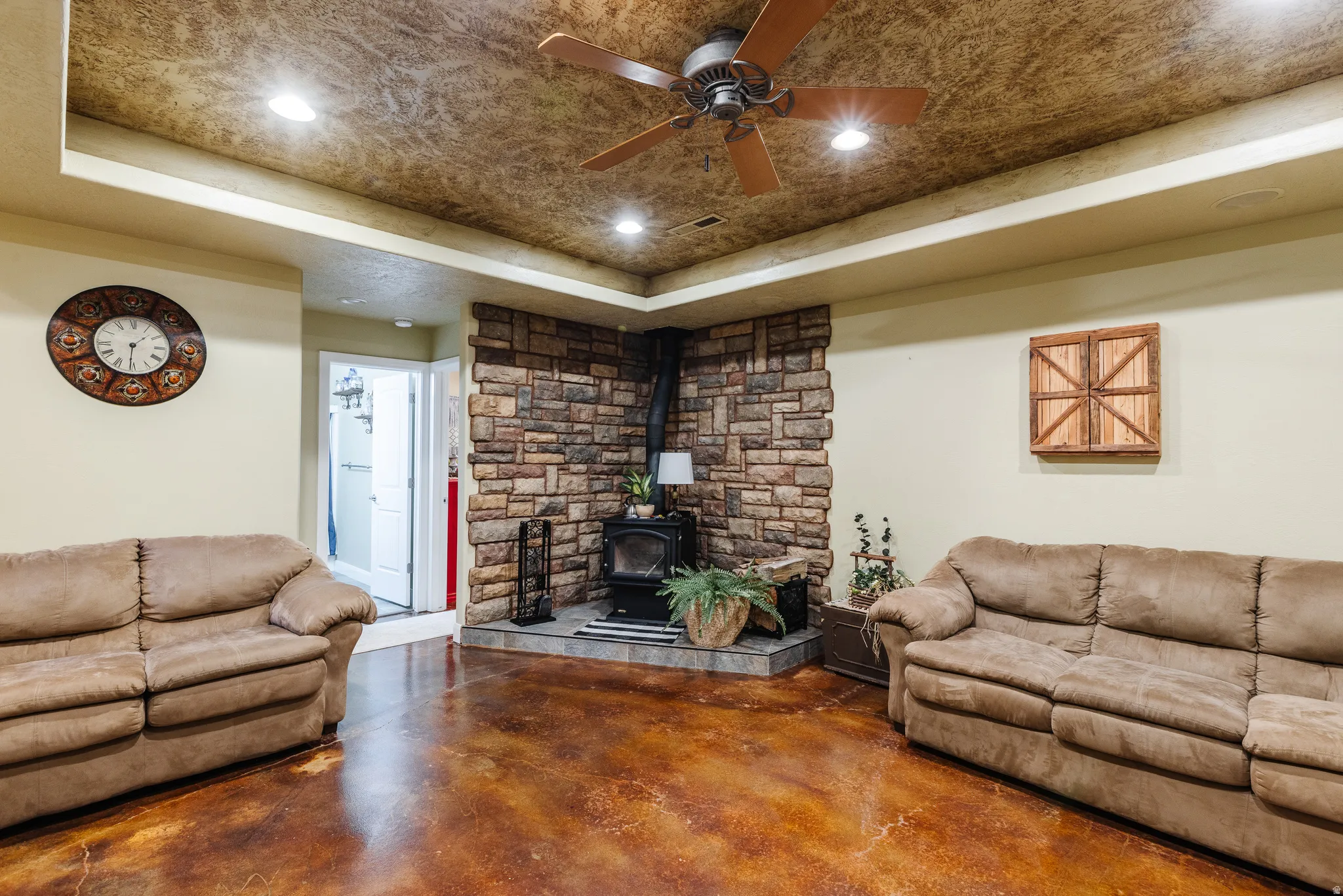 Living room with a raised ceiling, finished concrete flooring, a wood stove, recessed lighting, and ceiling fan