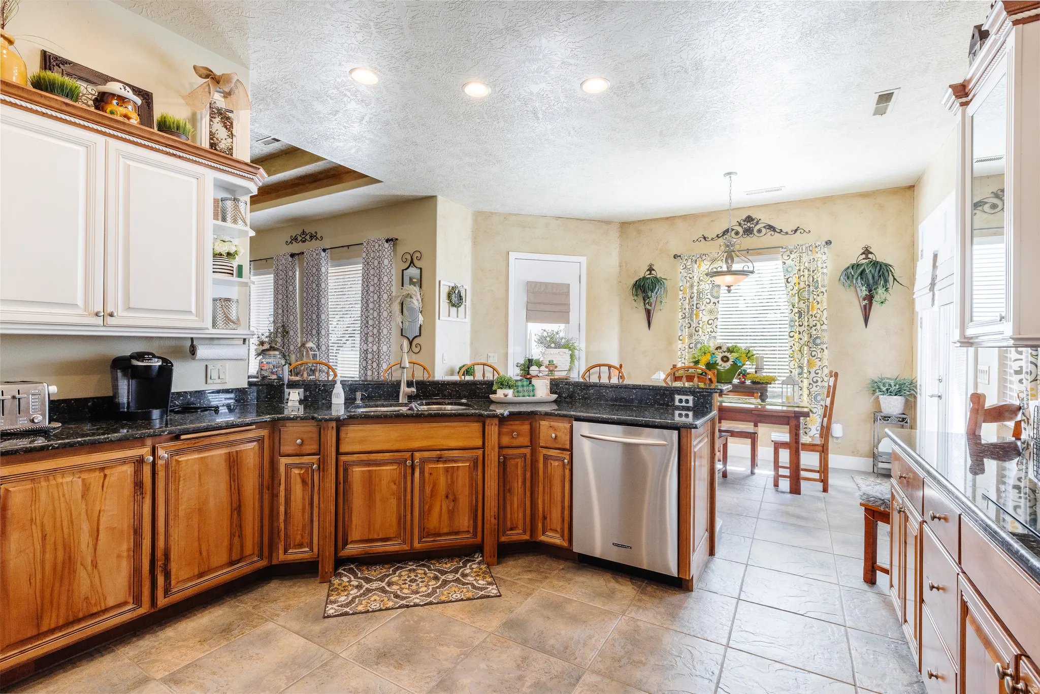 Kitchen featuring stainless steel dishwasher, dark stone counters, a peninsula, a textured ceiling, and wood finish cabinetry