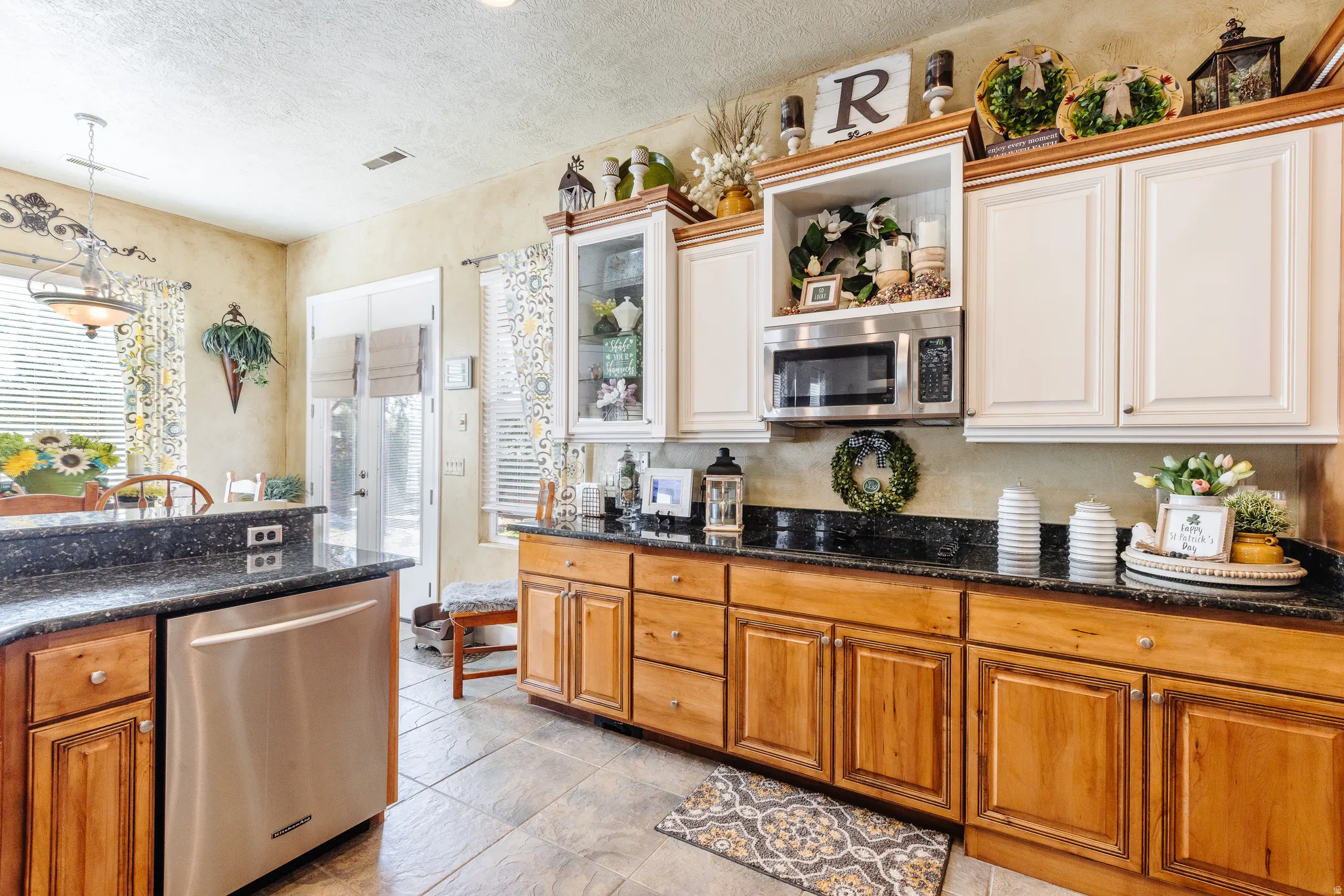 Kitchen with stainless steel appliances, wood finish cabinetry, dark stone counters, pendant lighting, and a textured ceiling