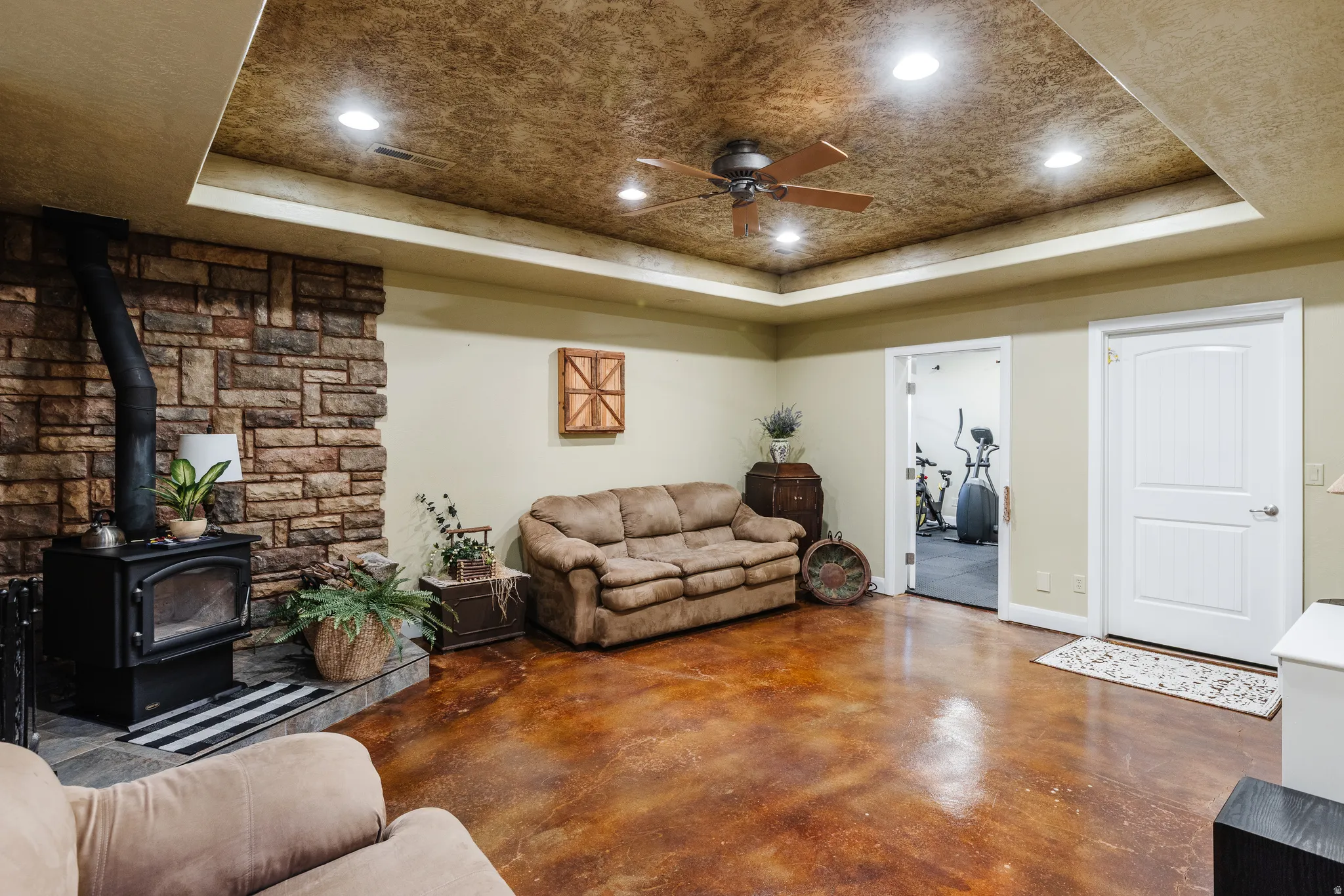 Living room with concrete floors, recessed lighting, a wood stove, ceiling fan, and a tray ceiling