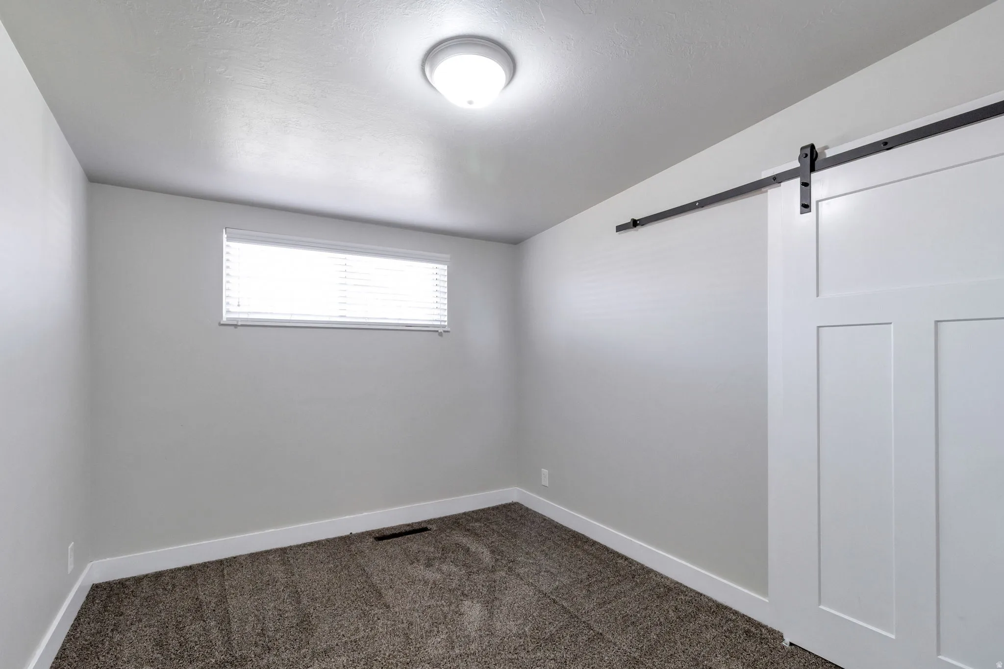 Empty room featuring a barn door and dark colored carpet