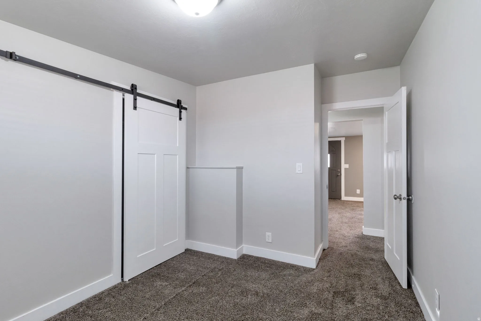 Unfurnished bedroom with a barn door and dark carpet