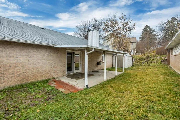 Back of property featuring a storage shed, a patio area, a yard, a chimney, and brick siding