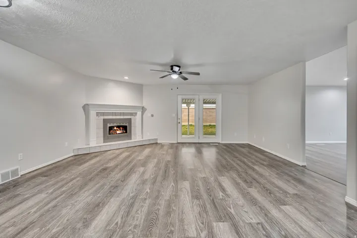 Unfurnished living room with light wood finished floors, a tiled fireplace, ceiling fan, a textured ceiling, and recessed lighting