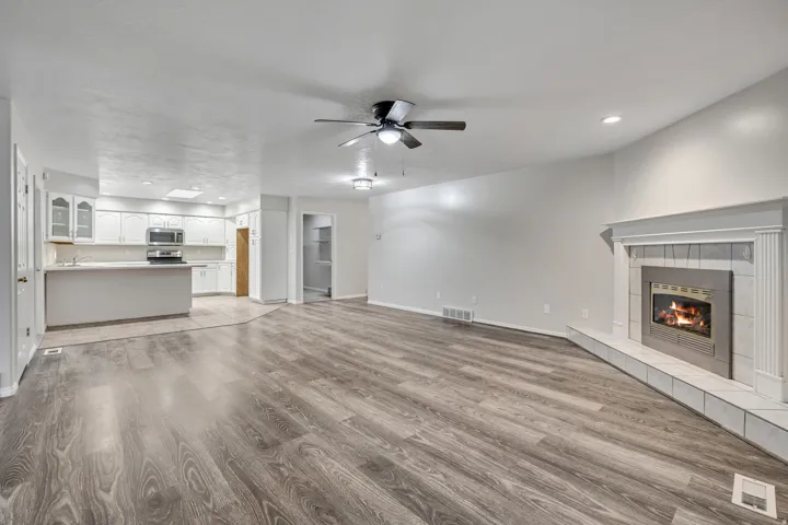 Unfurnished living room with light wood-type flooring, a ceiling fan, a tiled fireplace, and recessed lighting