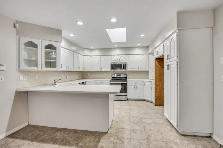 Kitchen with a skylight, a peninsula, glass fronted cabinets, light countertops, and stainless steel appliances