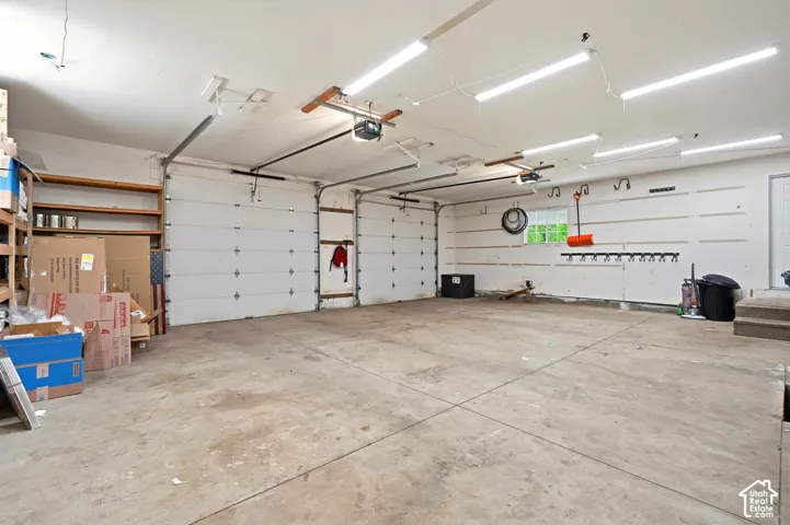 Spacious garage featuring two overhead doors with automatic openers, overhead fluorescent lighting, concrete flooring, and built-in shelving